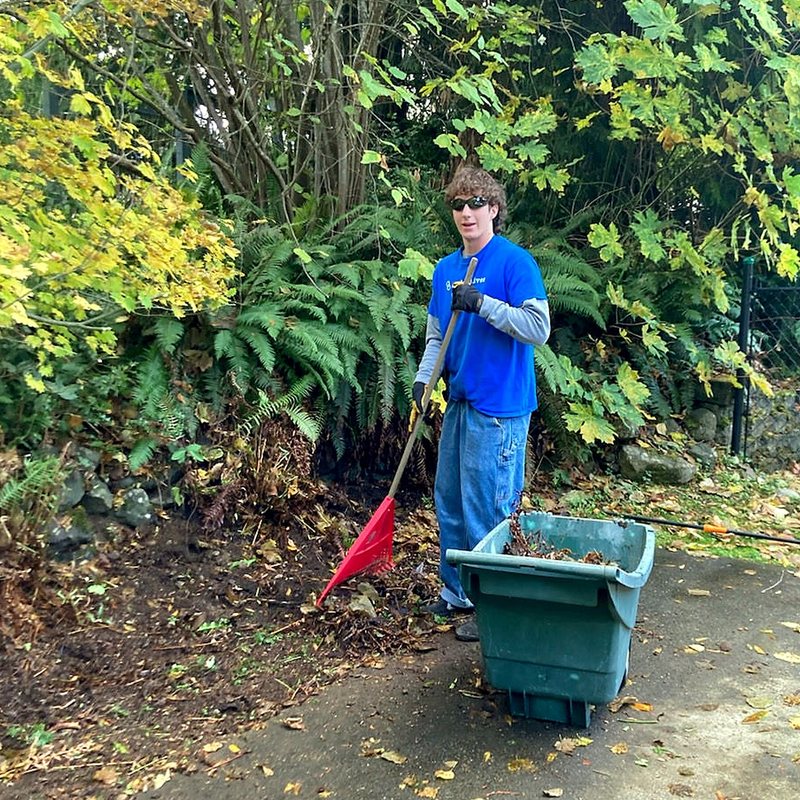 Linked Lives helper raking leaves by a garden cart