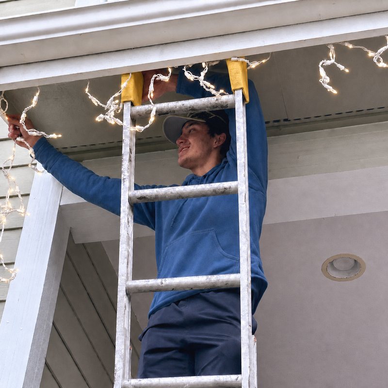 Linked Lives helper hanging Christmas lights from a ladder